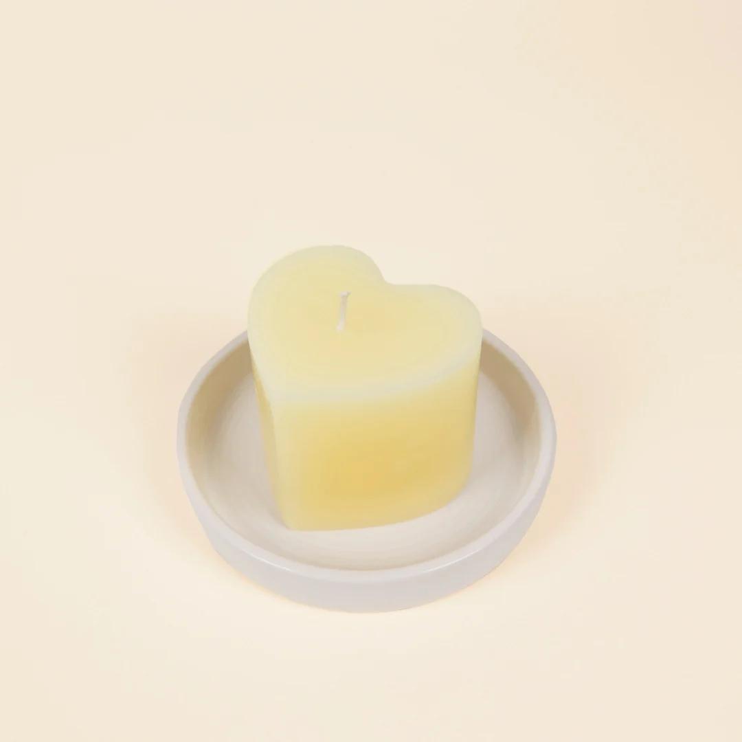 Heart-shaped candle on a white plate with a beige background
