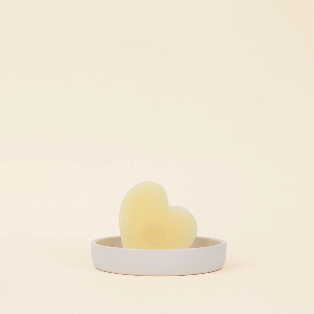 Heart-shaped yellow object on a small round gray dish against a beige background