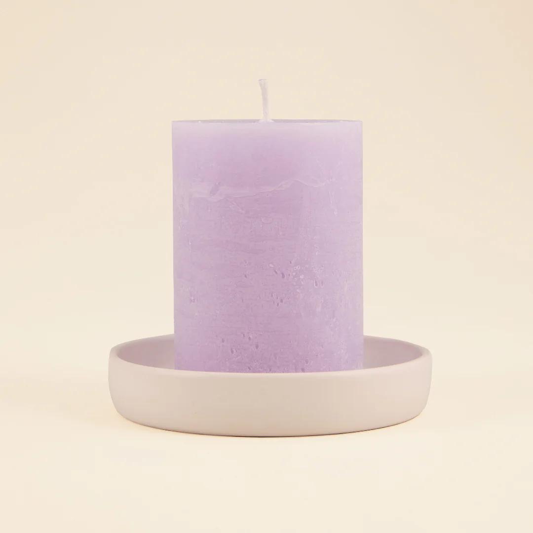 Purple candle on a white ceramic holder against a beige background