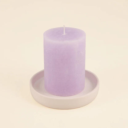 Purple candle on a white ceramic holder against a beige background