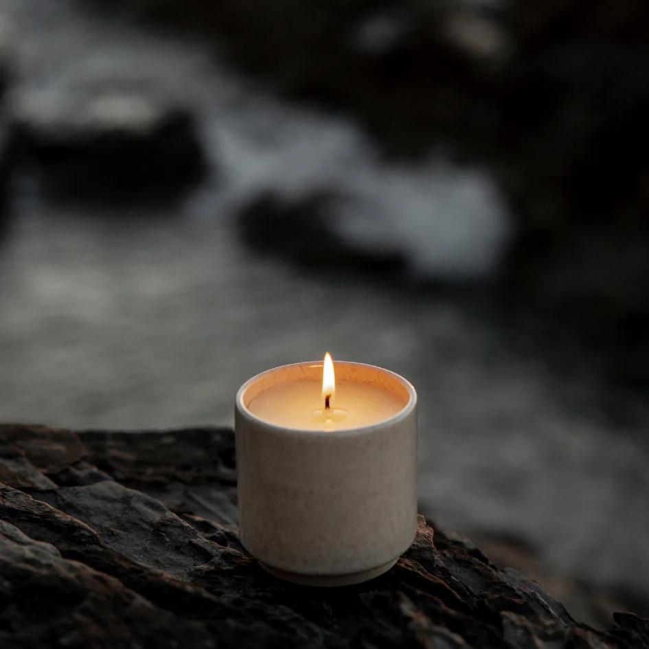 Candle in a textured container on a dark surface with a blurred natural background
