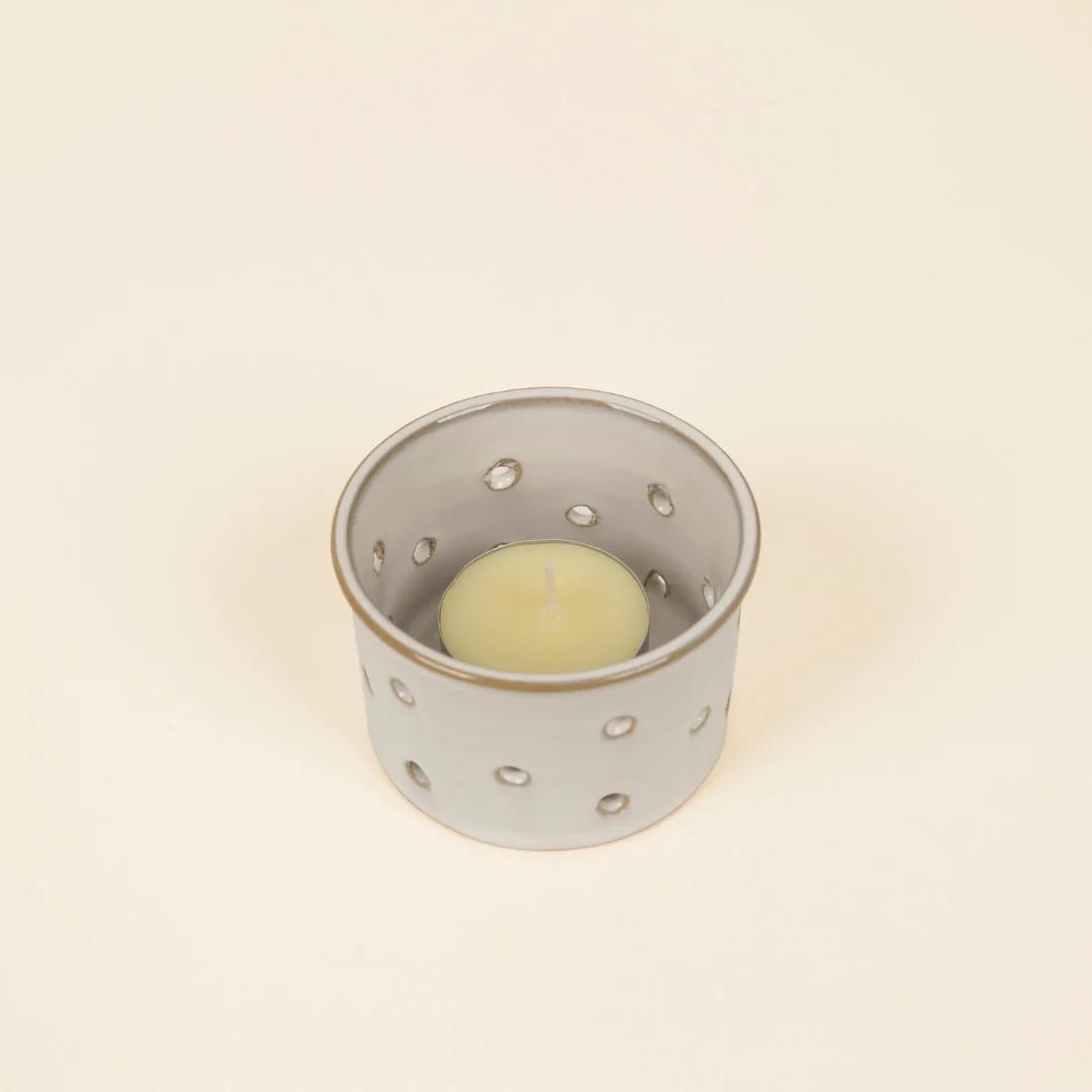 Ceramic candle holder with a small candle inside on a beige background