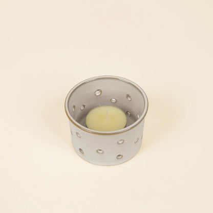 Ceramic candle holder with a small candle inside on a beige background