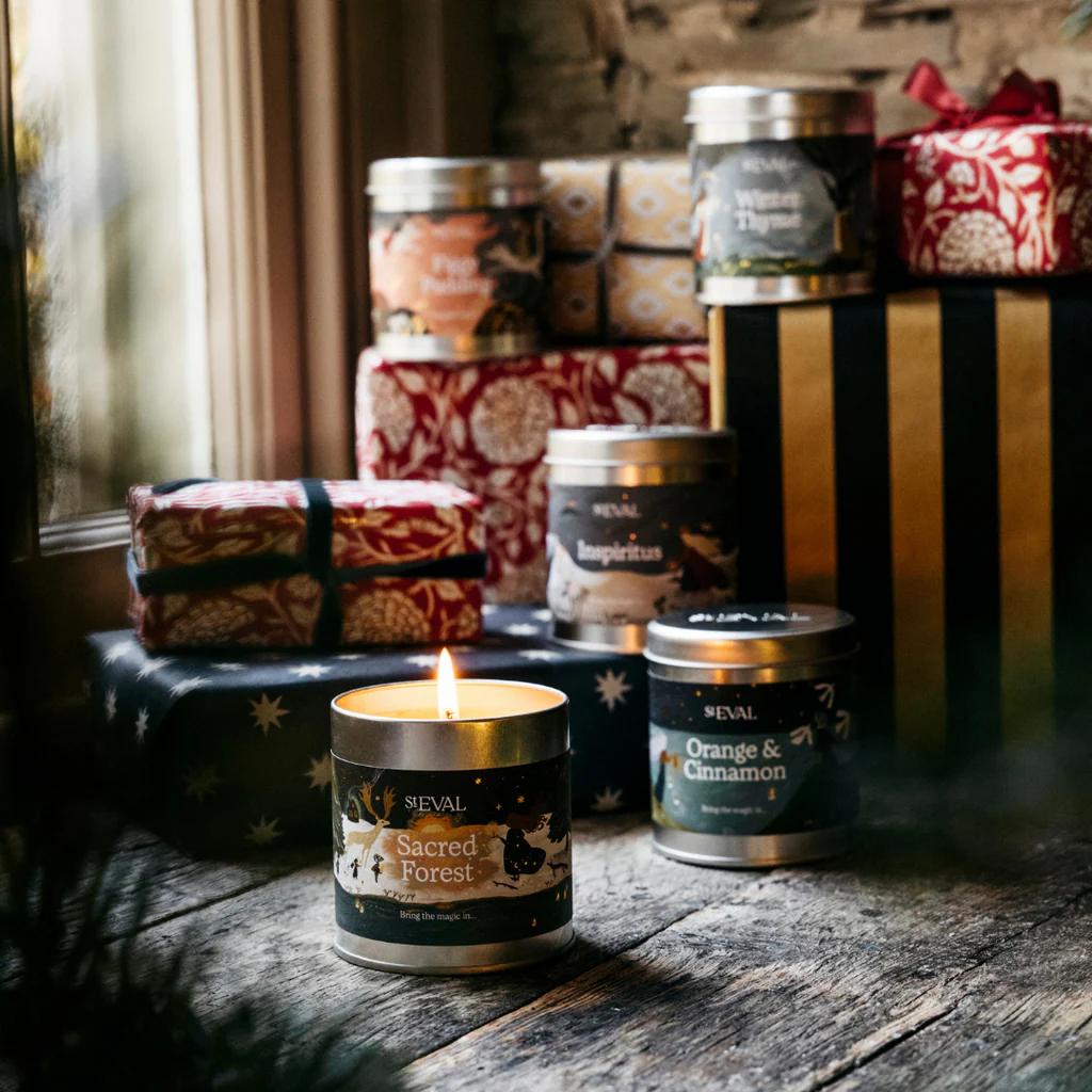 Candle and tins on a wooden surface with gift boxes in the background