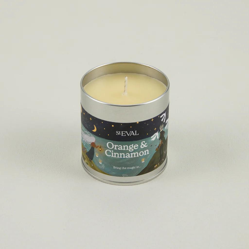 Candle in a tin labeled 'Orange & Cinnamon' by ST Eval on a light gray background