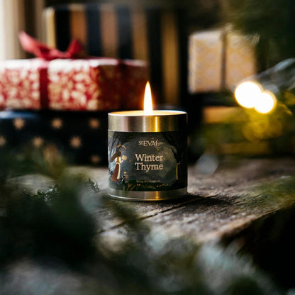Candle labeled 'Winter Thyme' by ST EVAL on a wooden surface with blurred gift and lights in the background