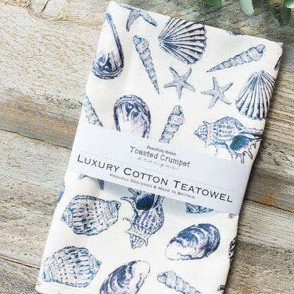 Luxury cotton teatowel with blue shell pattern on a wooden surface