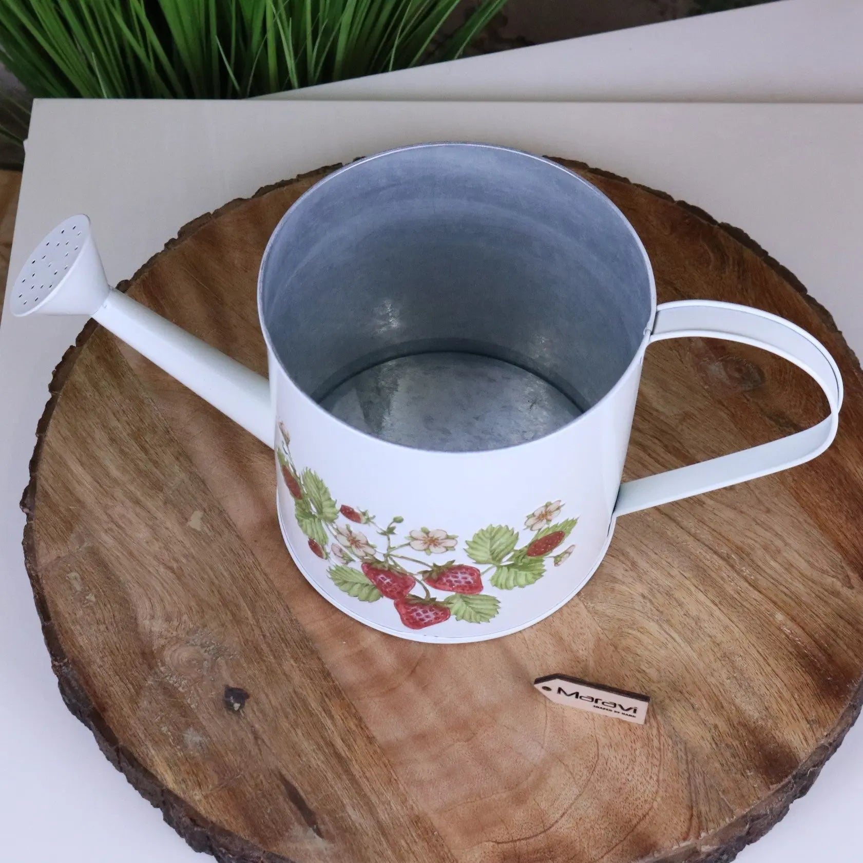 White mug with strawberry design on a wooden surface next to a watering can