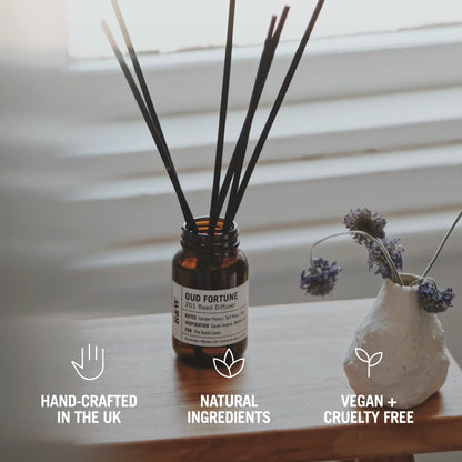 Reed diffuser with decorative vase on a wooden surface, featuring icons and text about product attributes.