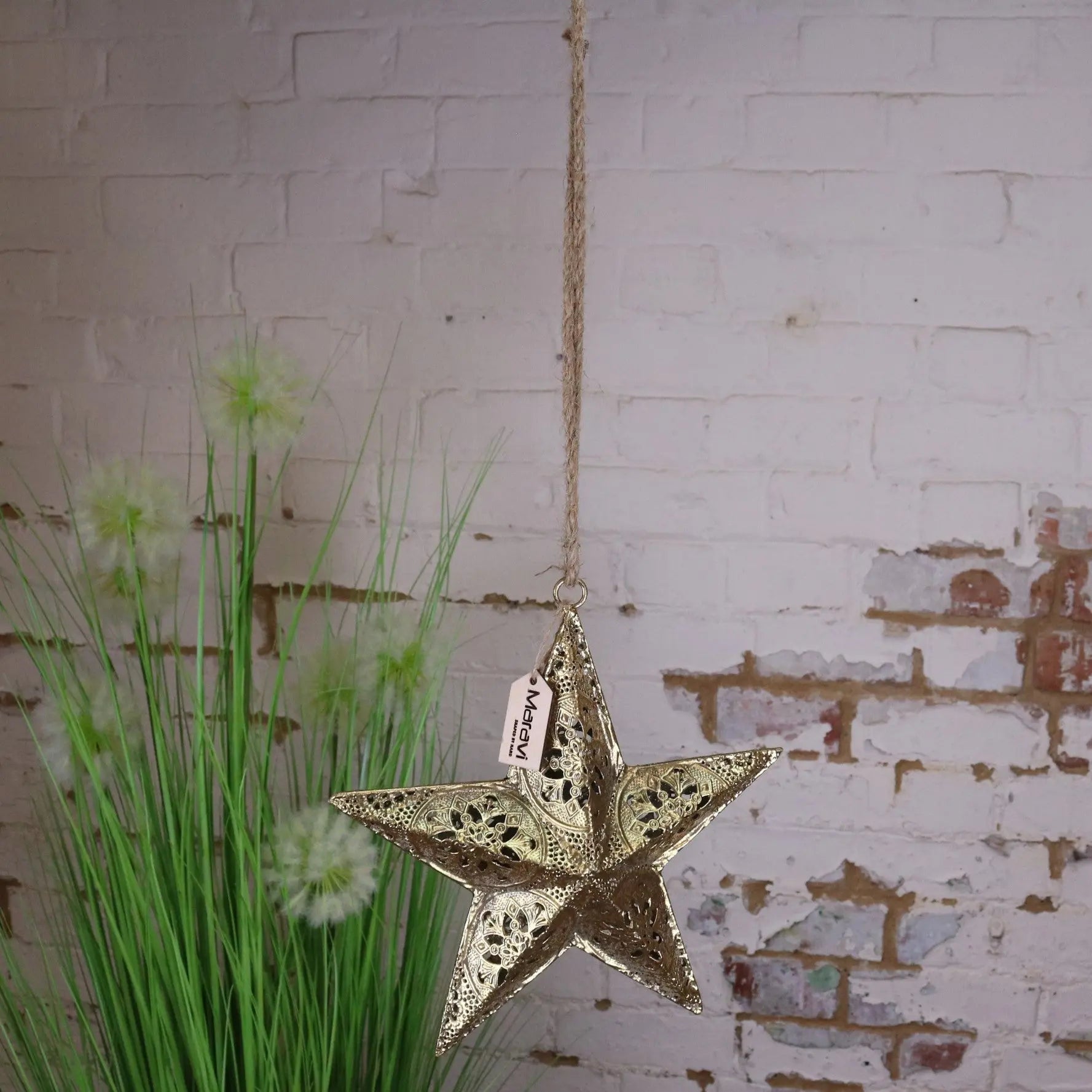 Decorative star hanging ornament with a tag against a rustic brick wall.