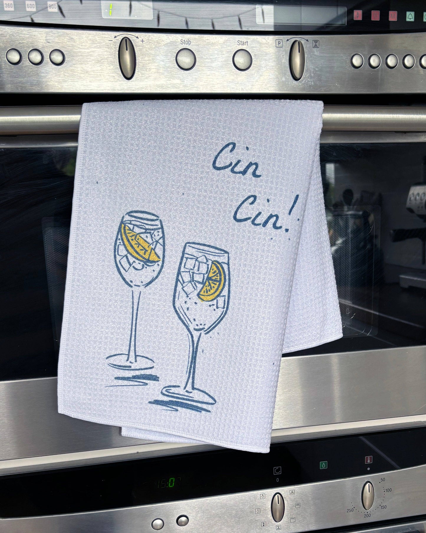 Kitchen towel with wine glass design and 'Cin Cin!' text hanging on a stove.