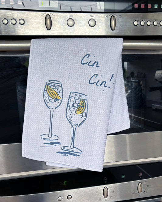 Kitchen towel with wine glass design and 'Cin Cin!' text hanging on a stove.