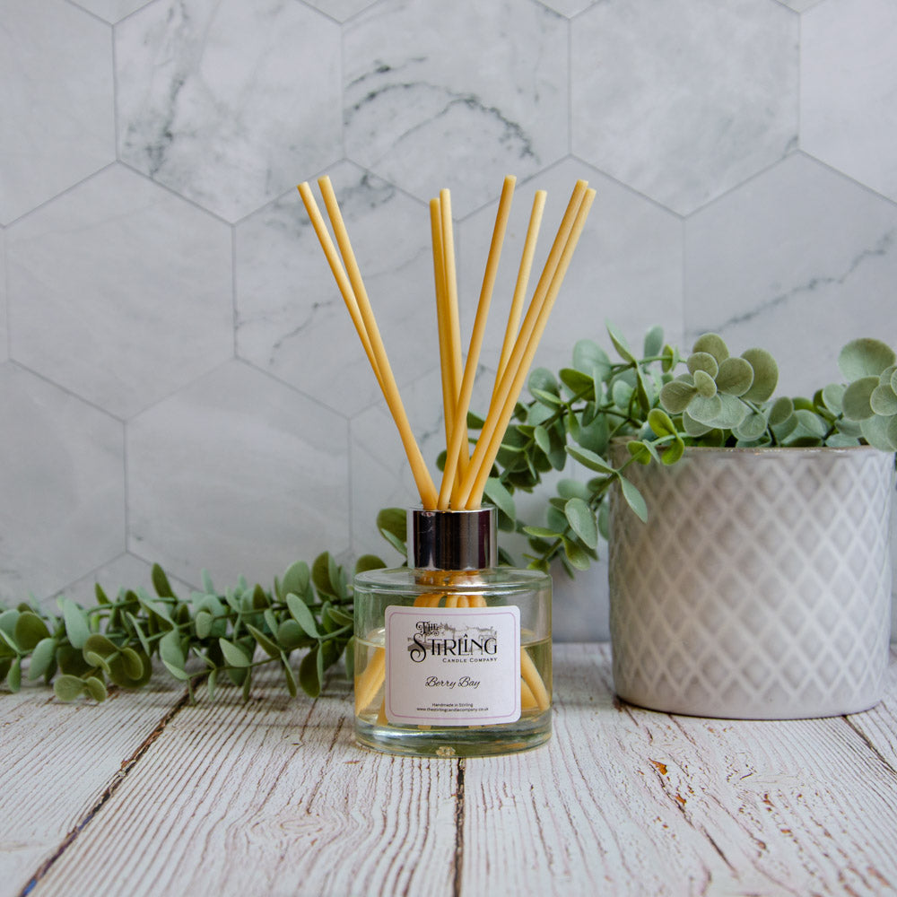 Reed diffuser with eucalyptus leaves on a wooden surface with a marble wall background